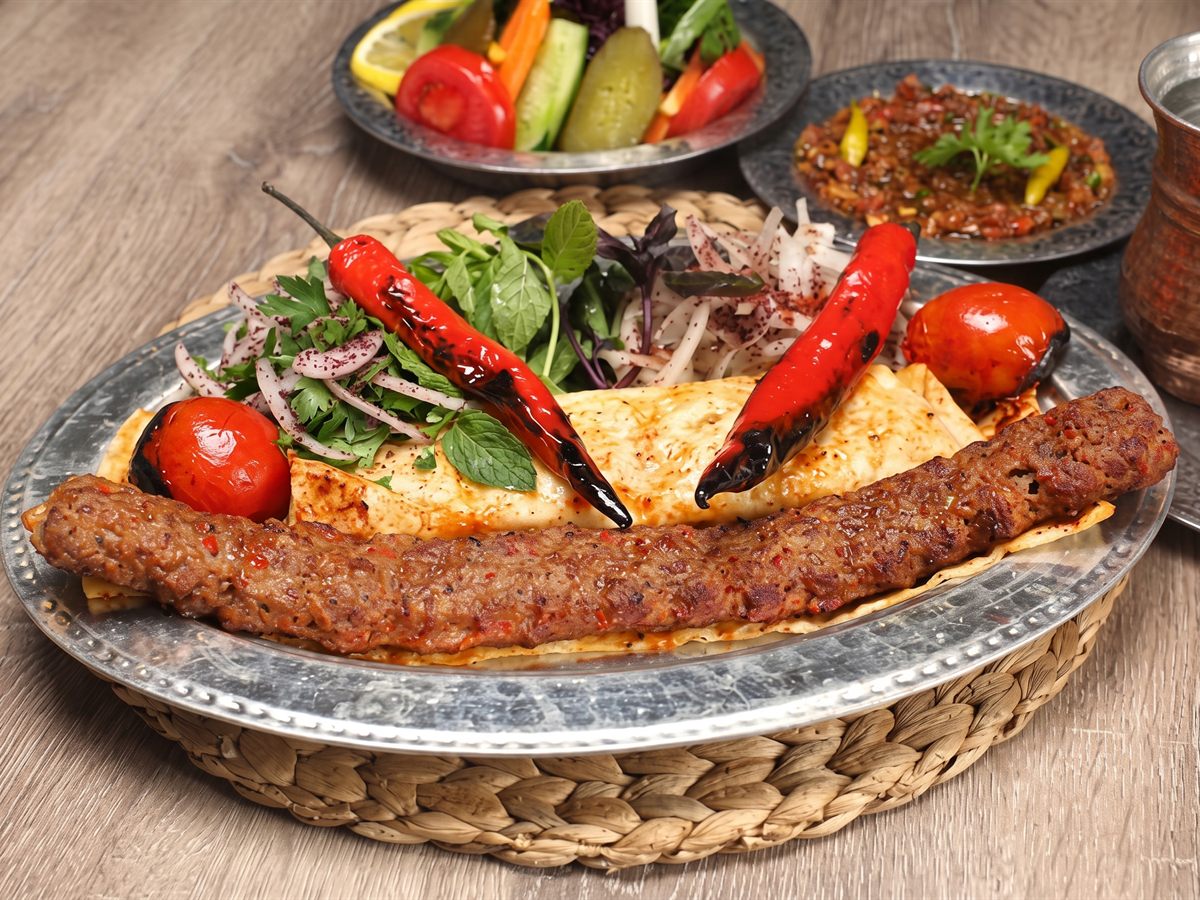 Lavaş üzerinde Adana kebap, közlenmiş kırmızı biber ve domates, sumaklı soğan salatası – Tutku Pide